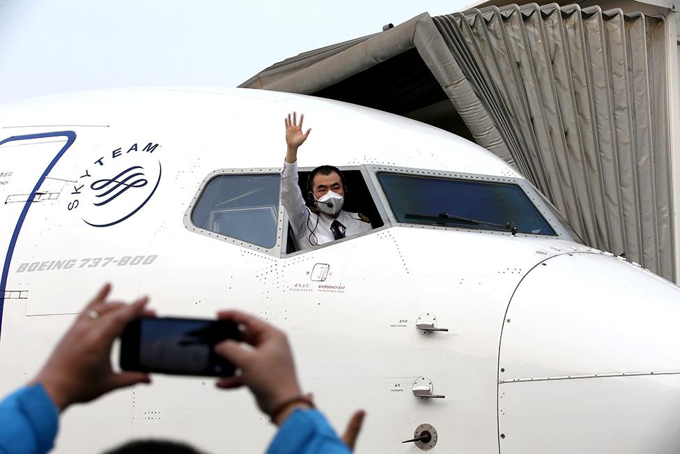 A pilot leans out of the cockpit window to wave goodbye