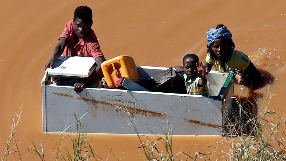 People holding on to some wooden furniture in Mozambique in flooded waters