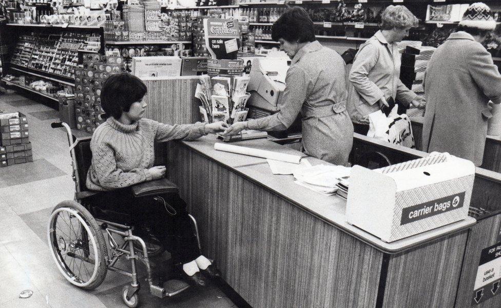 A woman from Banstead handing money over in a shop. She is a wheelchair user