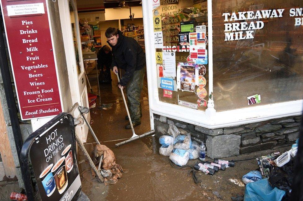 A shop worker in Glenridding sweeps flood waters out on to the street