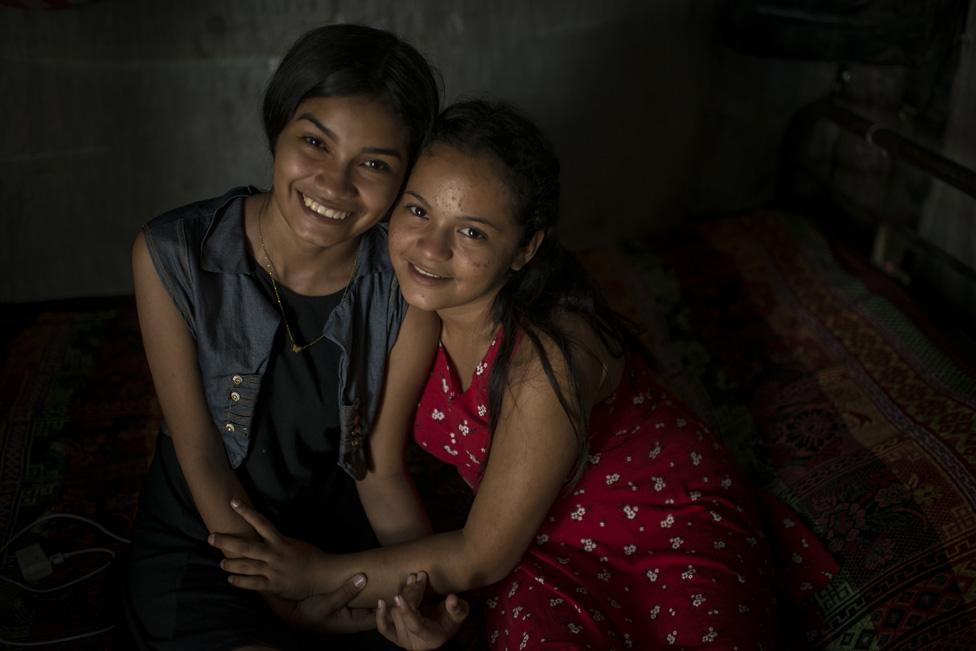 Sofía and Nahín hug sitting on the bed of the shack where they live