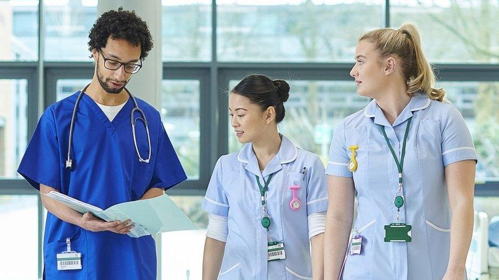 Three nurses walk along a ward