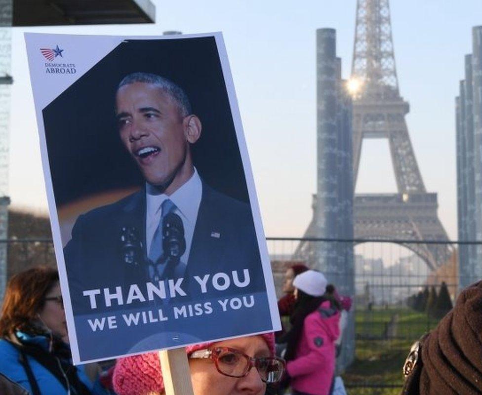 A demonstrator carries a sign featuring former U.S. President Barack Obama during a rally in solidarity with supporters of the Women's March in Washington and many other cities on 21 January 2017 in front of the Eiffel Tower in Paris, one day after the inauguration of the US President Donald Trump