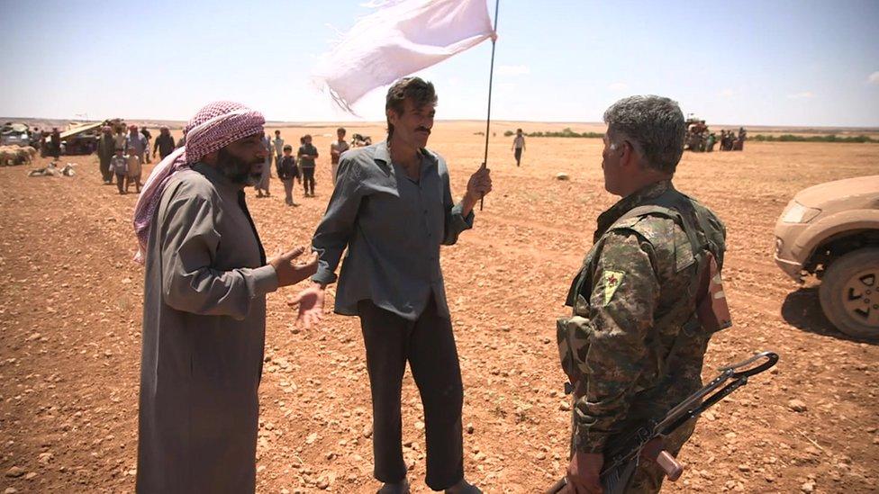 Kurdish fighter talking to displaced civilians in countryside outside Manbij