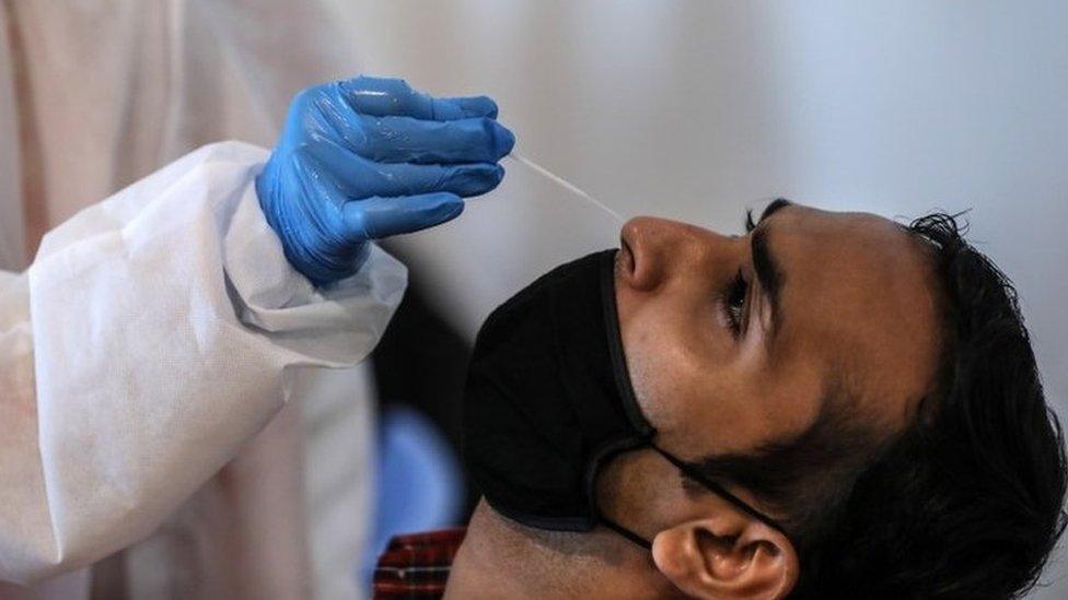 An Indian employee working in a mall, reacts as health worker takes a nasal swab sample to conduct his Rapid Antigen test for Covid-19 inside a mall in Mumbai, India