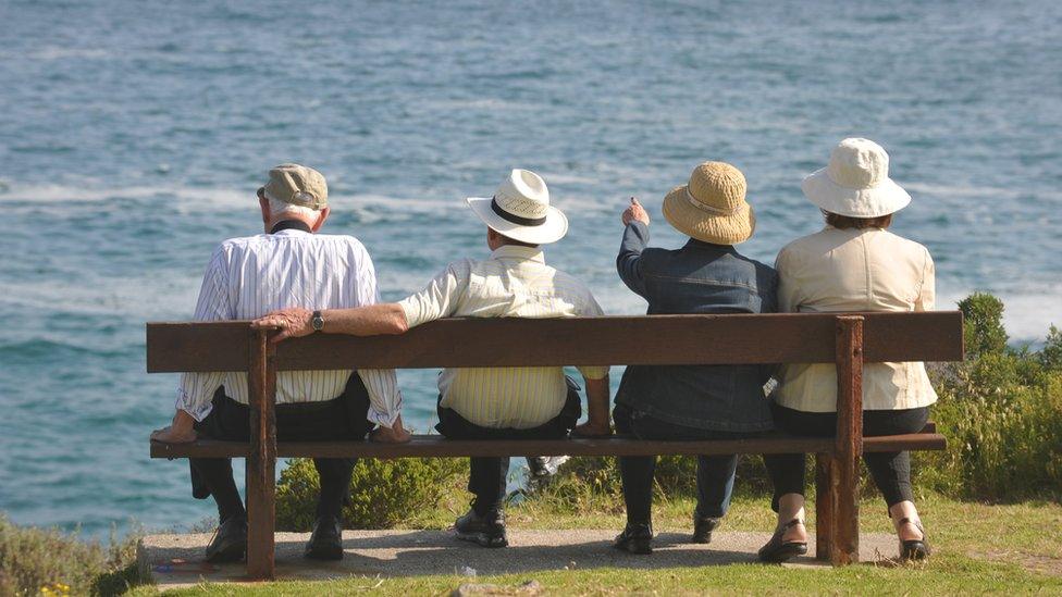 Two elderly couples sit on a bench and look out to sea