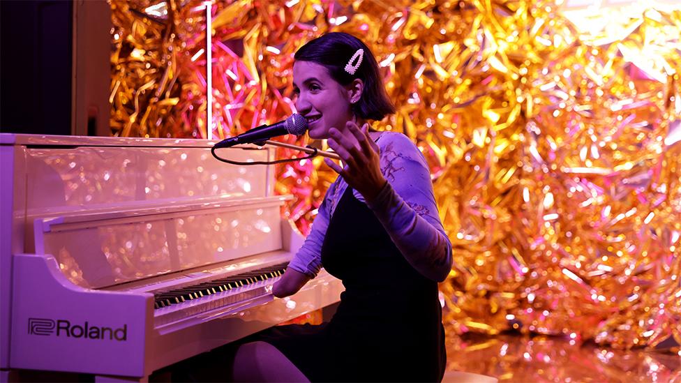 Victoria Canal playing the piano, in front of a glittery stage