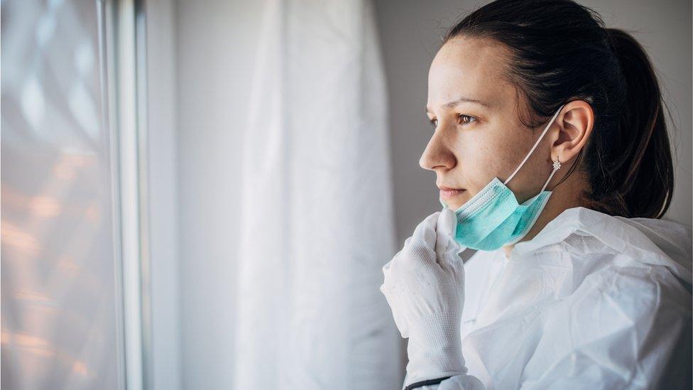 A concerned doctor in PPE looking out of a window