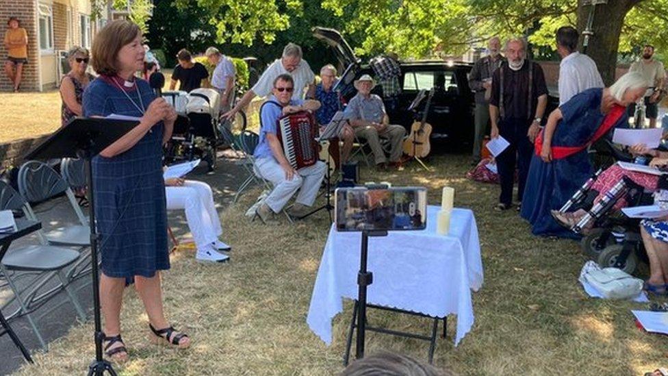 Woman preaching with musicians and spectators in the background