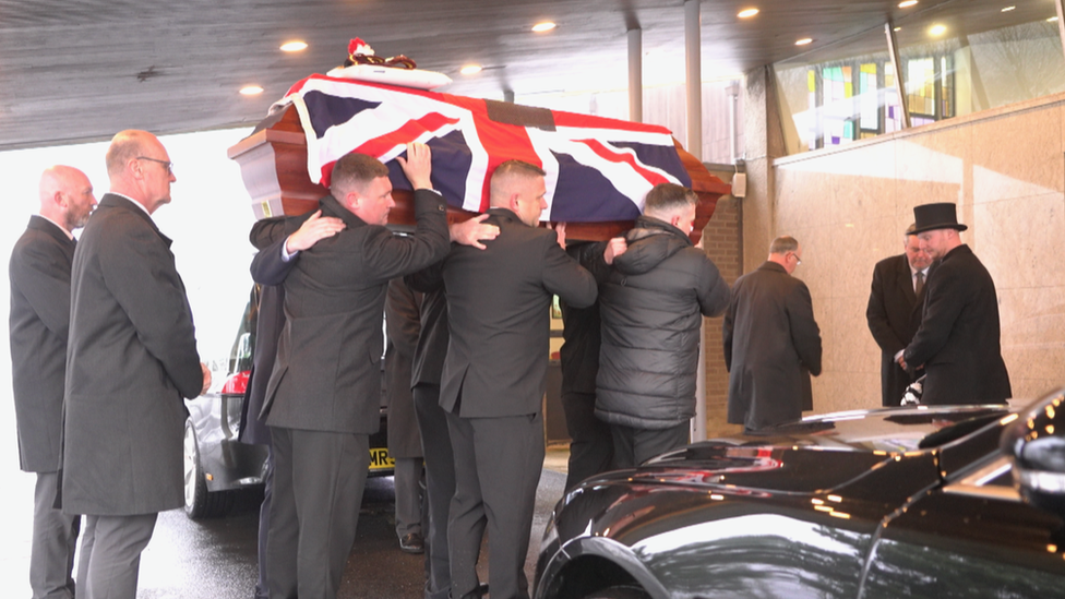 Pallbearers carry a coffin draped in a Union Jack flag