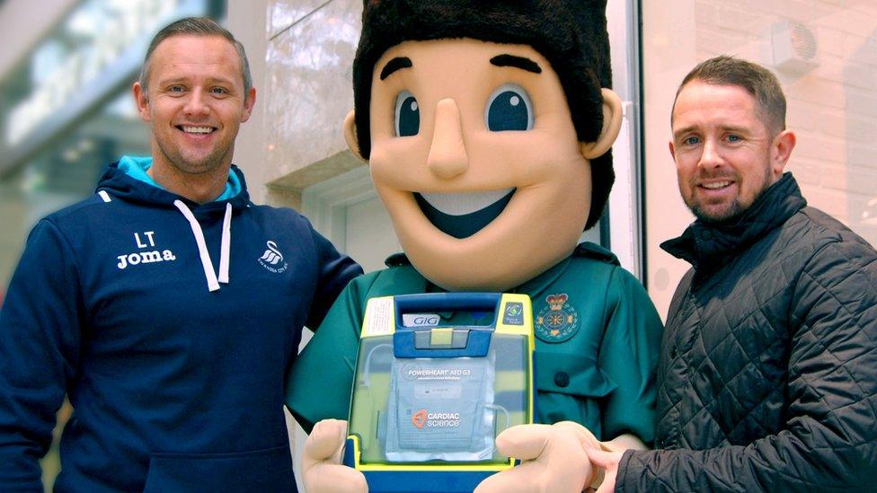 Lee Trundle, on the left, with Shane Williams and ambulance service mascot holding a defibrillator