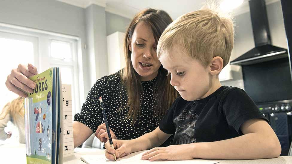 Little boy working on schoolbook with mother at home