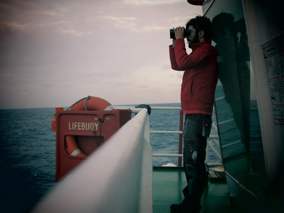 Volunteer looks out to sea through binoculars in daylight