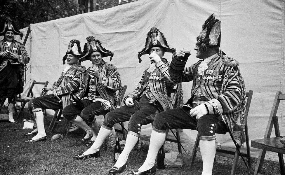 Royal footmen, dressed in glittering uniforms instead of their usual blue battledress raise the glasses in a toast to the Queen 1953