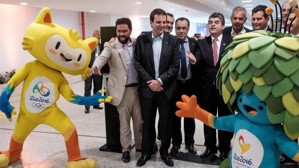 Rio de Janeiro's Mayor Eduardo Paes (C) stands between Olympic mascot Vinicius(L) and Paralympic mascot Tom (R) during the inauguration ceremony of the remodelled south wing of the Terminal 2 of the Antonio Carlos Jobim (Galeao) International Airport in Rio de Janeiro on May 19, 2016.