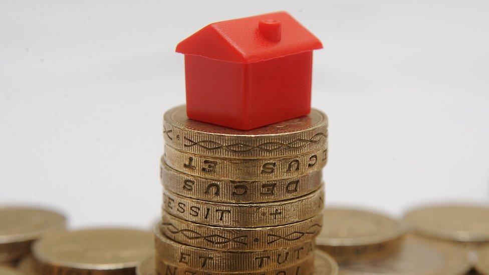 A plastic model of a house sitting on a pile of one pound coins