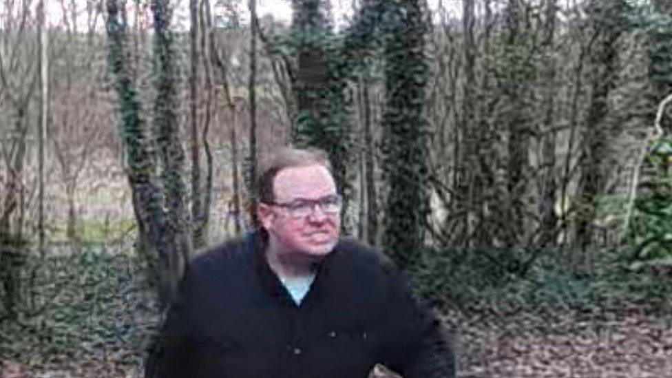 CCTV footage of a white man wearing a wearing glasses, a dark jacket and light blue t-shirt