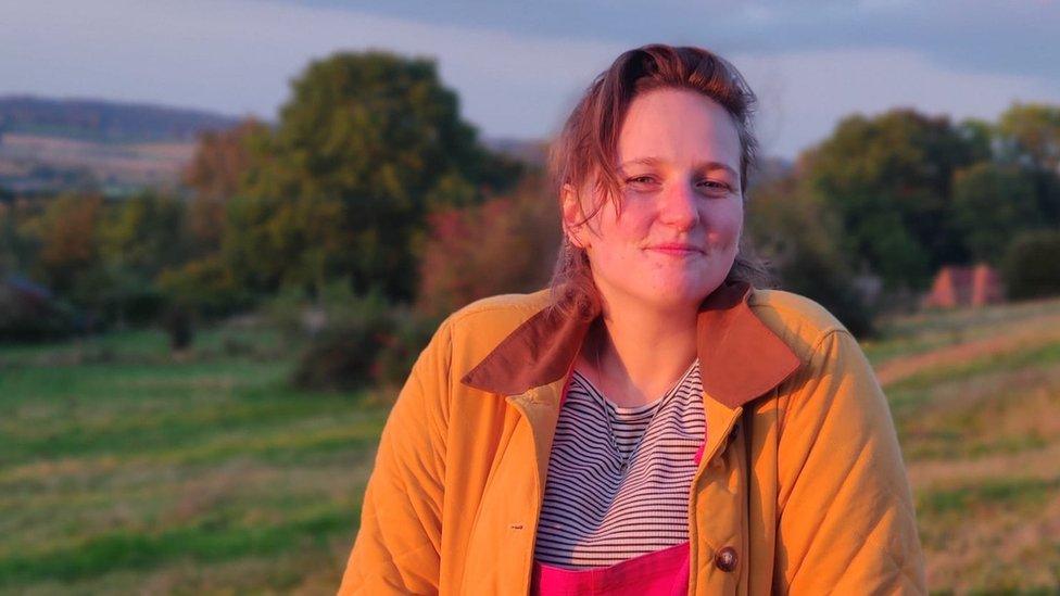 Megan Morgan smiling at the camera. She is wearing a yellow coat and a stripey t-shirt.