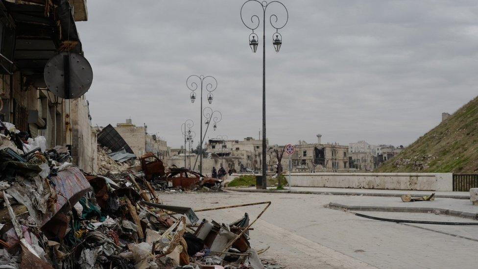 Ornate street lamps stand beside burnt out cars and piles of rubble