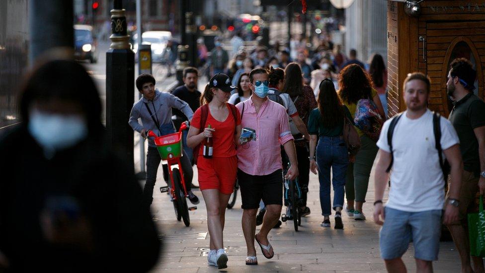 A man wearing a face mask walks along a busy Bridge Street outside Westminster Station as dusk falls at the end of a warm spring day in London