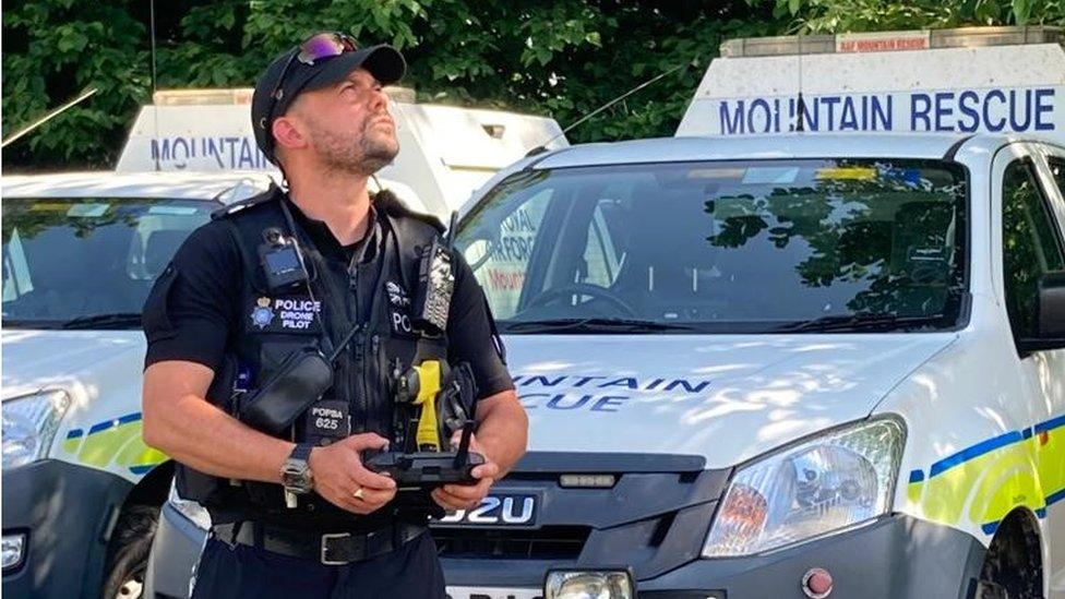 Police drone pilot looking up to the sky at scene of search