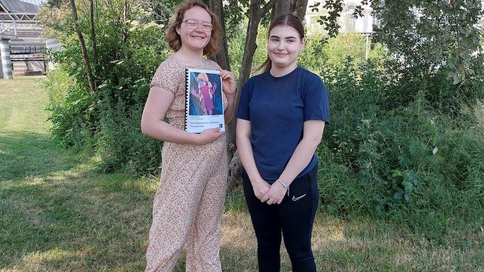 Rebecca and Fay, stood in front of a tree, Rebecca is holding a folder which contains a petition asking to make it illegal to discriminate against those in care