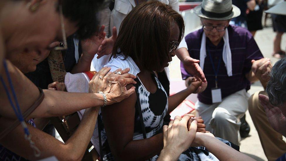 Delores Qualls prays with visitors in front of the Emanuel AME Church on the one-month anniversary of the July 2015 mass shooting in Charleston, South Carolina