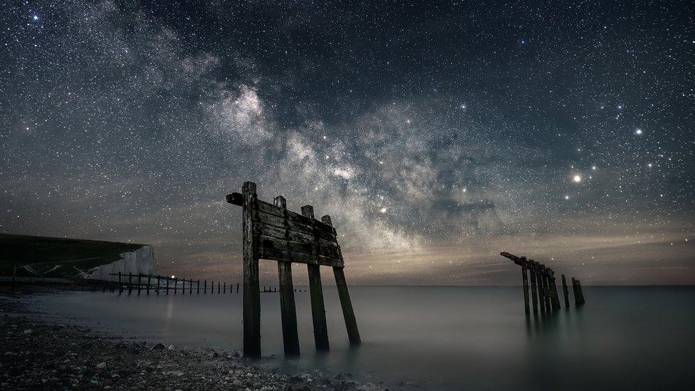 The Milky Way is shown in a night sky with the Seven Sisters cliffs in the background, the sea and stony beach in the foreground