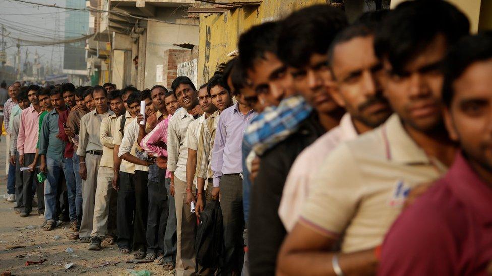 Indians stand in a queue to deposit and exchange discontinued currency notes outside a bank in New Delhi, India