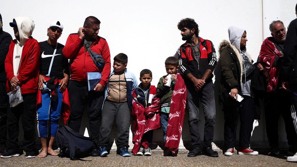 Migrants stand in line as they wait for the bus to be taken for processing, in Dungeness, on the southeast coast of England.