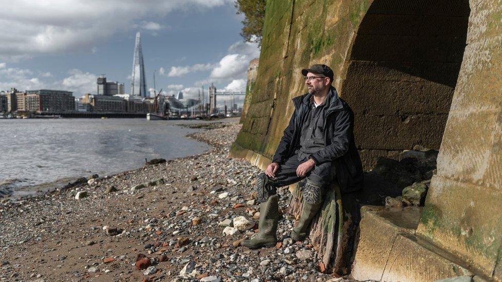 Malcom Russell sitting on an arch on the foreshore of the Thames