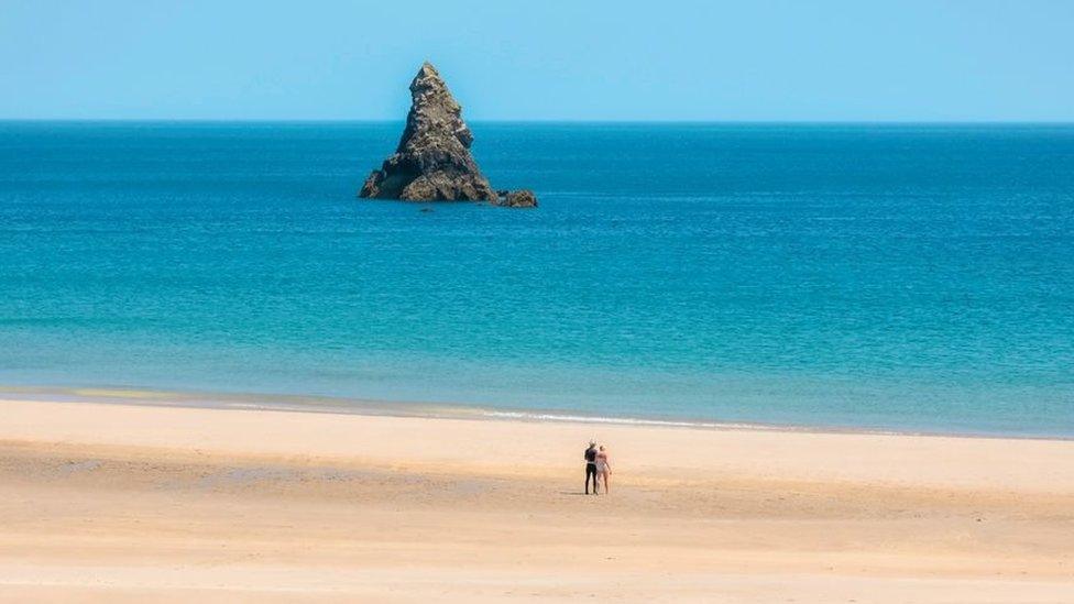 A rock stands out of a deep blue sea on a clear sky