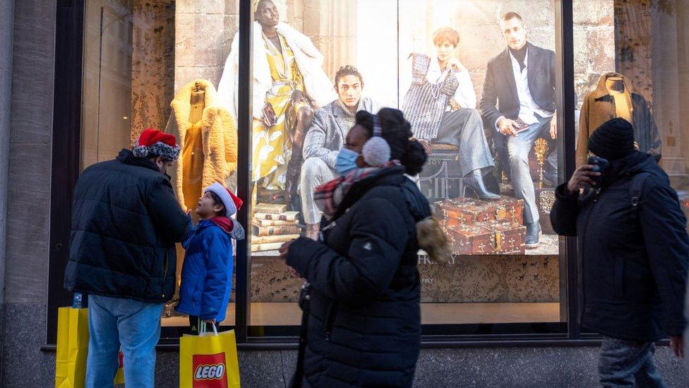 A father and son wearing Santa Claus hats and holding Lego shopping bags stand on Fifth Avenue