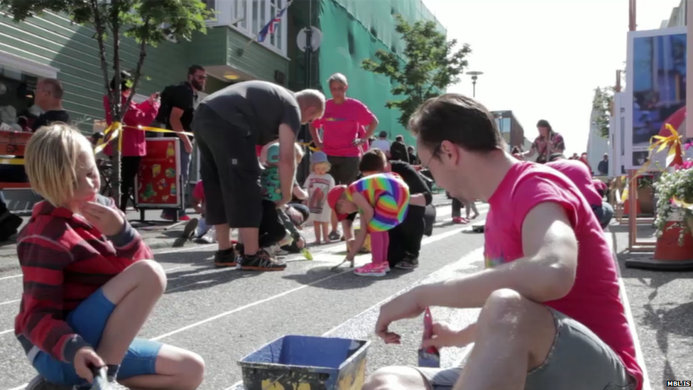 Children and adults sat on the street painting it by hand