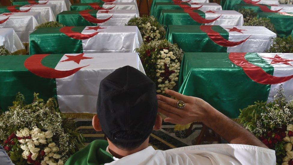 An Algerian man pays respect in front of the national flag-draped coffins containing the remains of 24 Algerian resistance fighters at the Palais De La Culture Moufdi Zakaria a day after they were flown in from France - July 2020