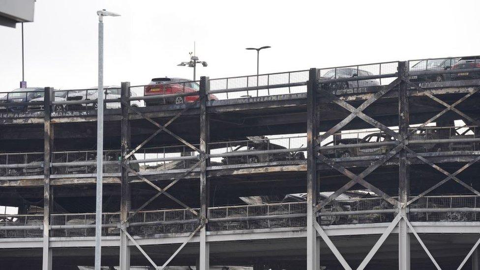 A view showing the top level of the car park and some levels below. Burned out cars and collapse of floors can be seen.