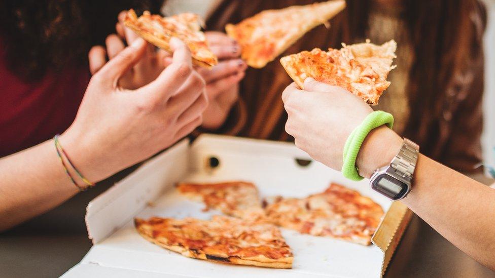 A box of pizza being shared by teenagers