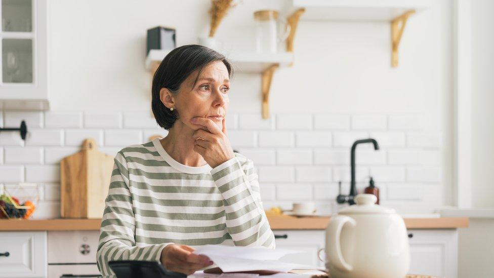 Woman next to teapot reading energy bill