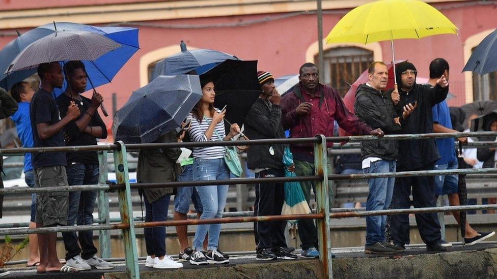 Crowd of people with umbrellas look on at the collapsed bridge