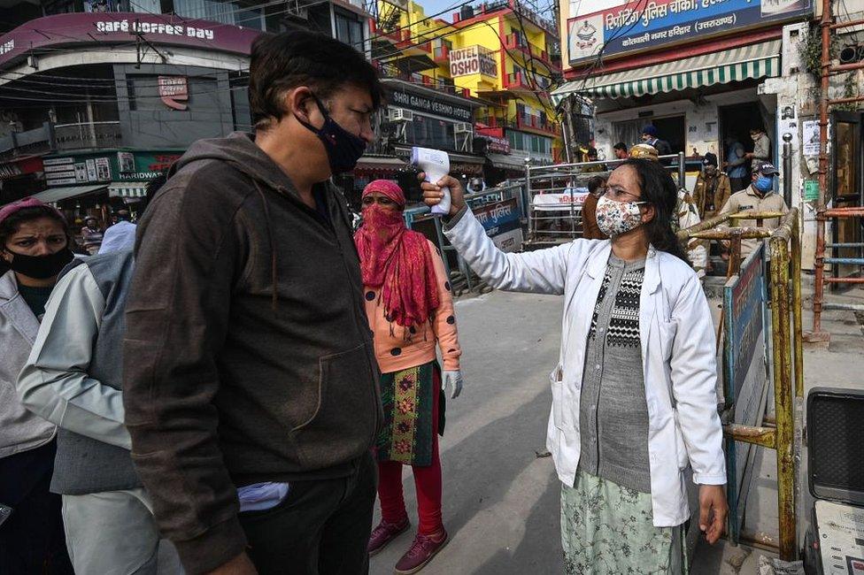 A volunteer (R) checks the temperature of devotees who arrive to take a holy dip in the waters of the River Ganges during Makar Sankranti, a day considered to be of great religious significance in the Hindu mythology, on the first day of the religious Kumbh Mela festival in Haridwar on 14 January 2021