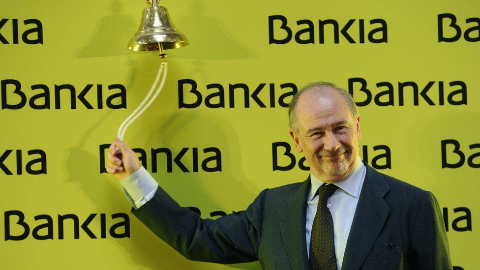 Rodrigo Rato, smiling, stands in fromt of yellow placard reading "Bankia! and rings the bell at Madrid's stock exchange on July 20, 2011 to mark the start of Bankia's listing