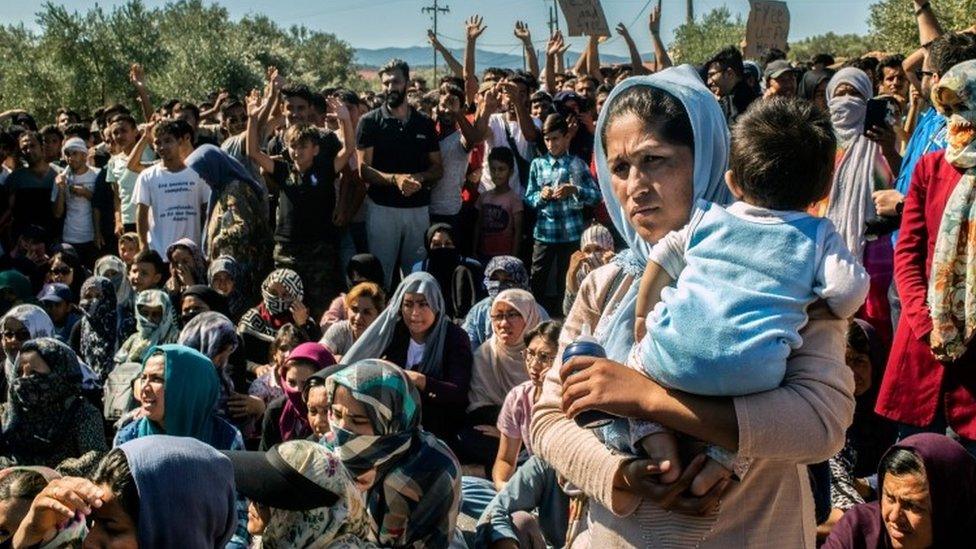 A woman holds a baby as refugees and migrants take part in a demonstration against their living conditions at the Moria camp on the island of Lesbos