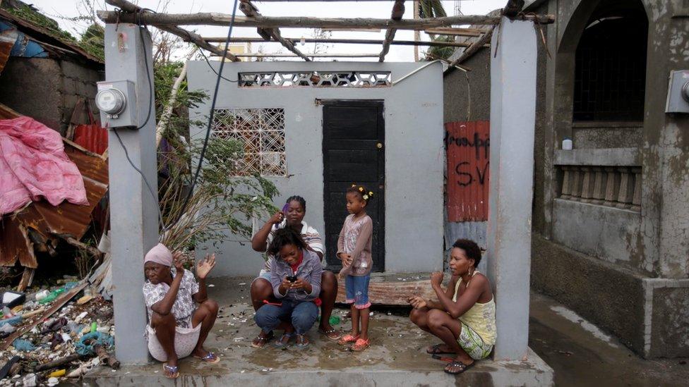 Family sit at entrance to damaged home in Les Cayes, Haiti, on 5 October 2016