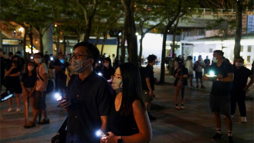 People gather with their phone lights on near Victoria Park, June 2021