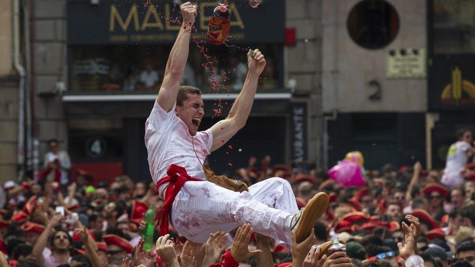 A partygoer in Pamplona is held aloft by the crowd, showered by the red Sangria spiralling through the air above him