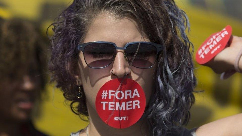 A supporter of Dilma Rousseff, her mouth covered with a sticker that reads in Portuguese; "Temer out", takes part in a protest in front of the National Congress, where the impeachment trial of Rousseff is taking place, in Brasilia, Brazil, Tuesday, Aug. 30, 2016.