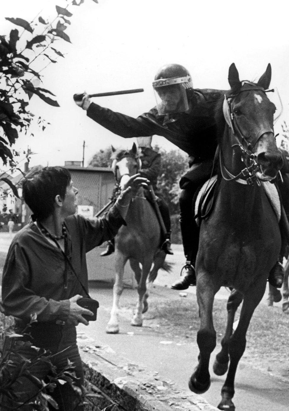 Police officer on horseback aims truncheon at woman in crowd