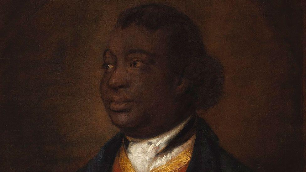 Thomas Gainsborough, Ignatius Sancho, 1768. It is a close-up of his head and shoulders. He is looking towards his right and has his hair pulled back in a short ponytail. He is wearing a dark jacket over a yellow waistcoat with a white neck cloth tucked into it.