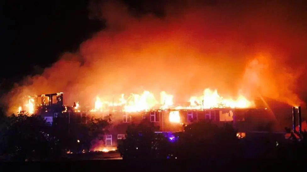 A large building with its roof engulfed in flames at night.