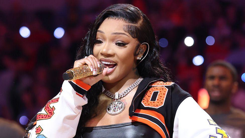 GloRilla in a colourful jacket singing into a gold-studded microphone at the WNBA All-Star Game